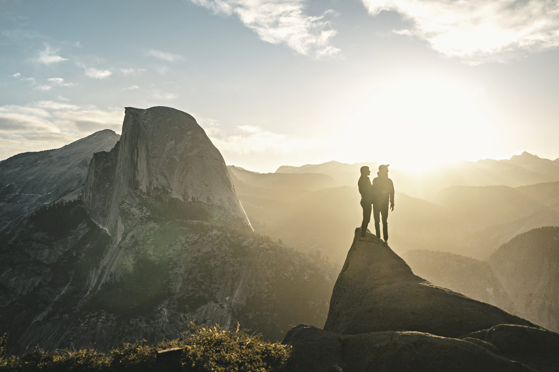 Two people enjoying a happy relationship stand on top of a mountain in Yosemite National Park.
