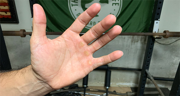 A man's hand in front of a heavy barbell in the gym, showing signs of calluses from weightlifting.
