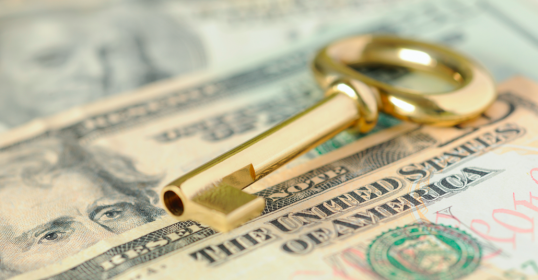 In this image, a golden key rests on a pile of US dollar bills.
