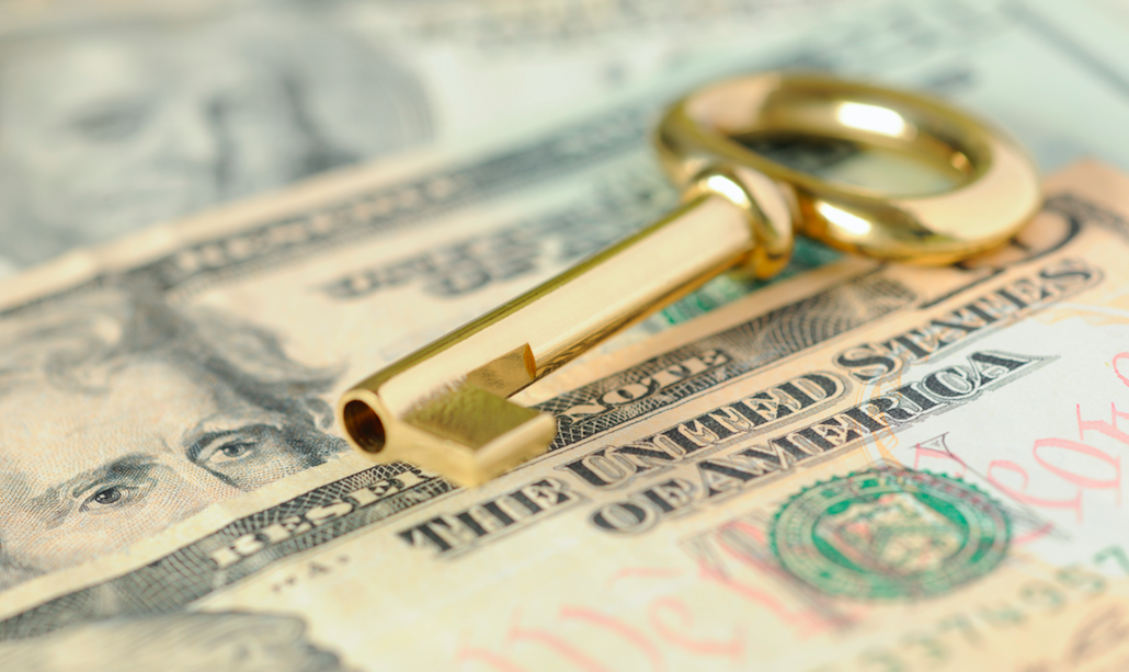 In this image, a golden key rests on a pile of US dollar bills.