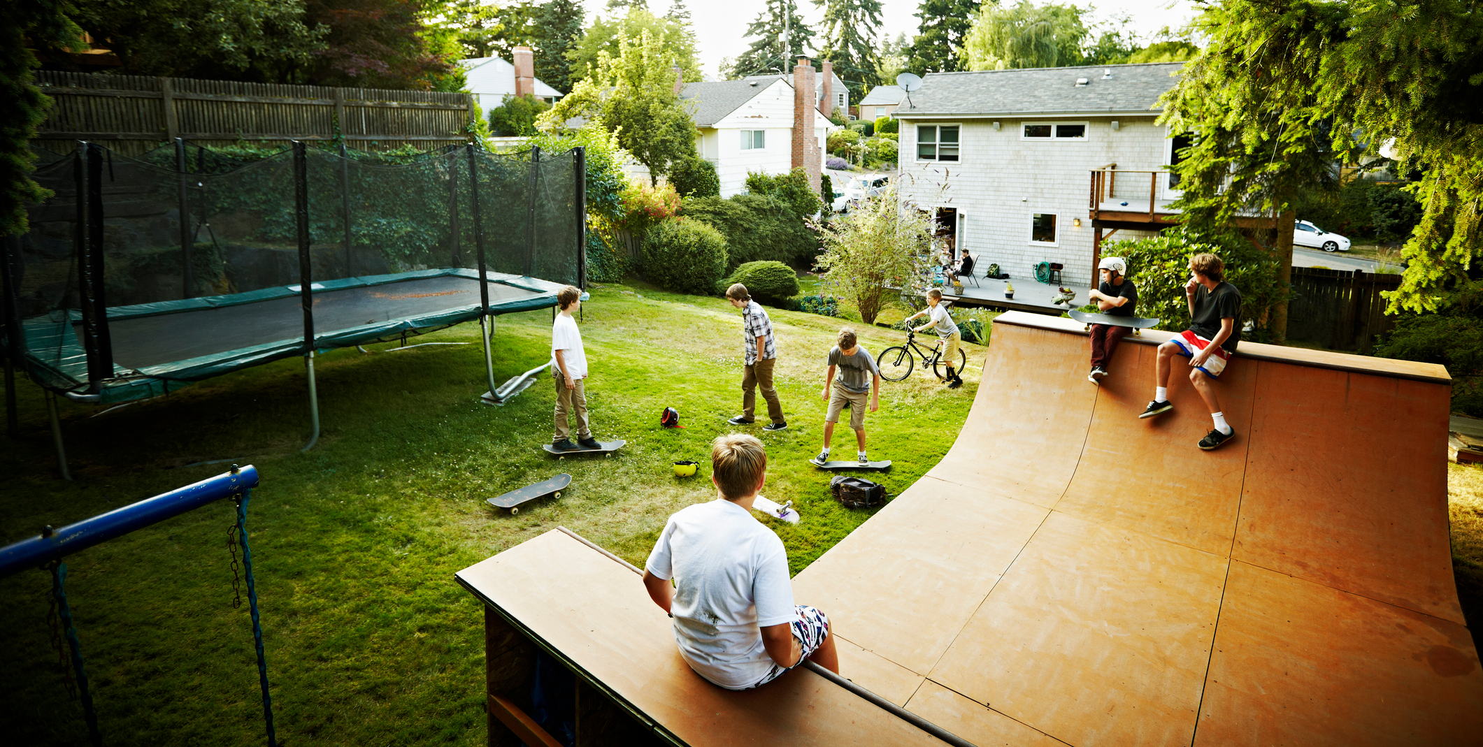 A group of kids create playing on a skateboard ramp in a neighborhood backyard.