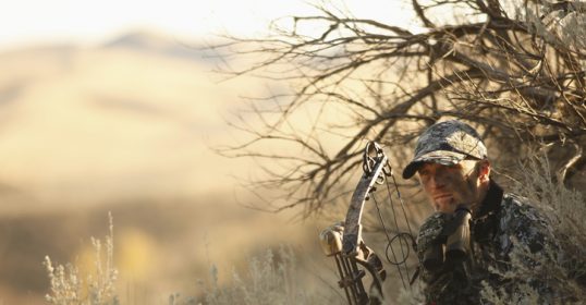A man with a bow and arrow hunting in the brush.