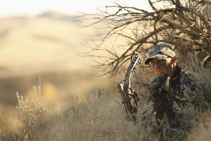 A man with a bow and arrow hunting in the brush.