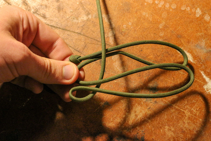 Step 4: Hold onto the base of your loops, take the long end of your paracord and bring it under the bottom loop, and over the top loop.