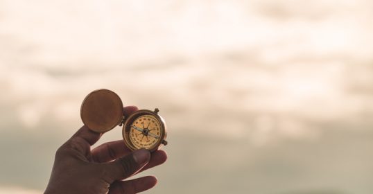 A person holding a compass in front of a mountain, searching for their calling in life.