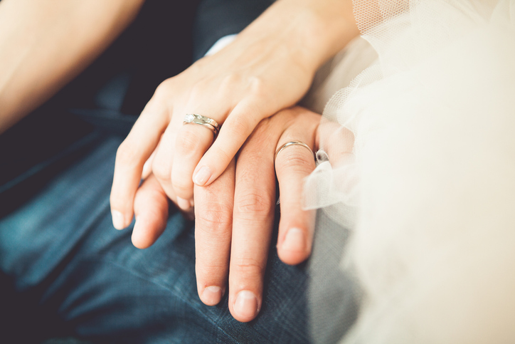 A bride and groom's hands strengthen each other's wedding rings.
