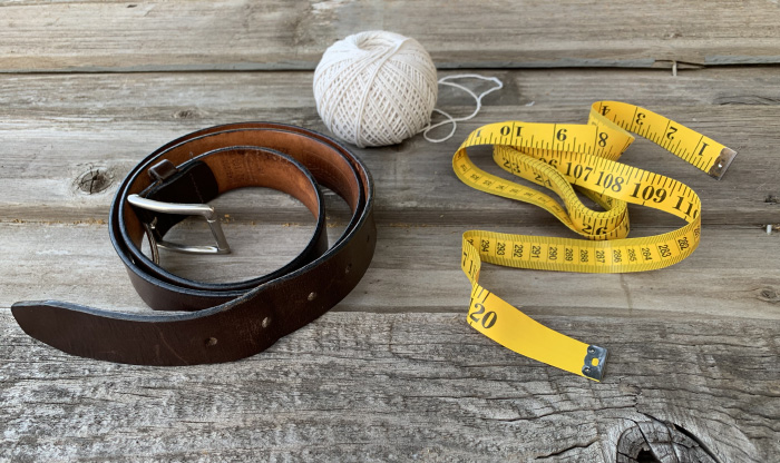 Belt, measuring tape and thread displayed on table.