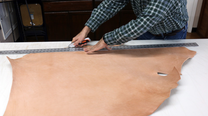 Man cutting the Strap of Leather with the help of scale and cutter.