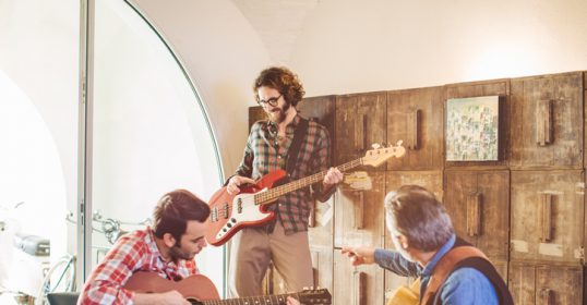 A group of men, around the same age, playing guitars in a room.