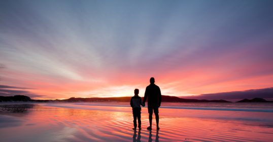 A man and a woman standing on a beach at sunset, cultivating gratitude.