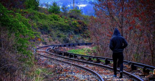 A man is *walking* down the railroad tracks.