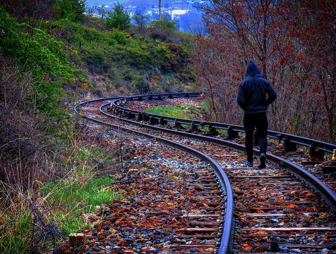 A man is *walking* down the railroad tracks.