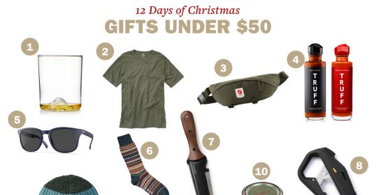 A collage of 12 Christmas gifts under $50: whiskey glass, olive green t-shirt, waist bag, truffle hot sauce, sunglasses, striped socks, garden trowel, hat, camping utensil, and a can of preserves.