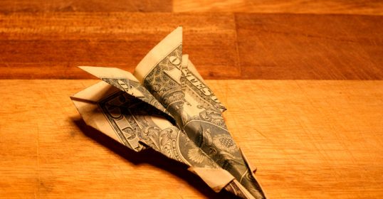 An origami paper airplane, inspired by a fighter jet, resting on a wooden table.