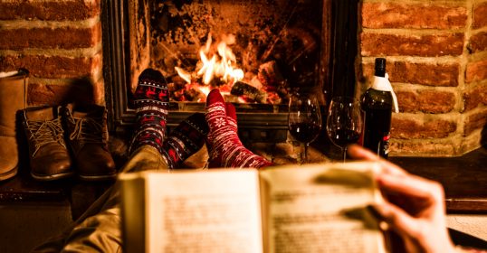 Two people cozily reading a book by the fireplace.