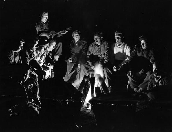 A group of men sitting around a campfire, enjoying the lost pleasures of group singing.