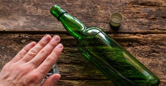 A hand next to a green bottle on a wooden table, reflecting on life lessons.