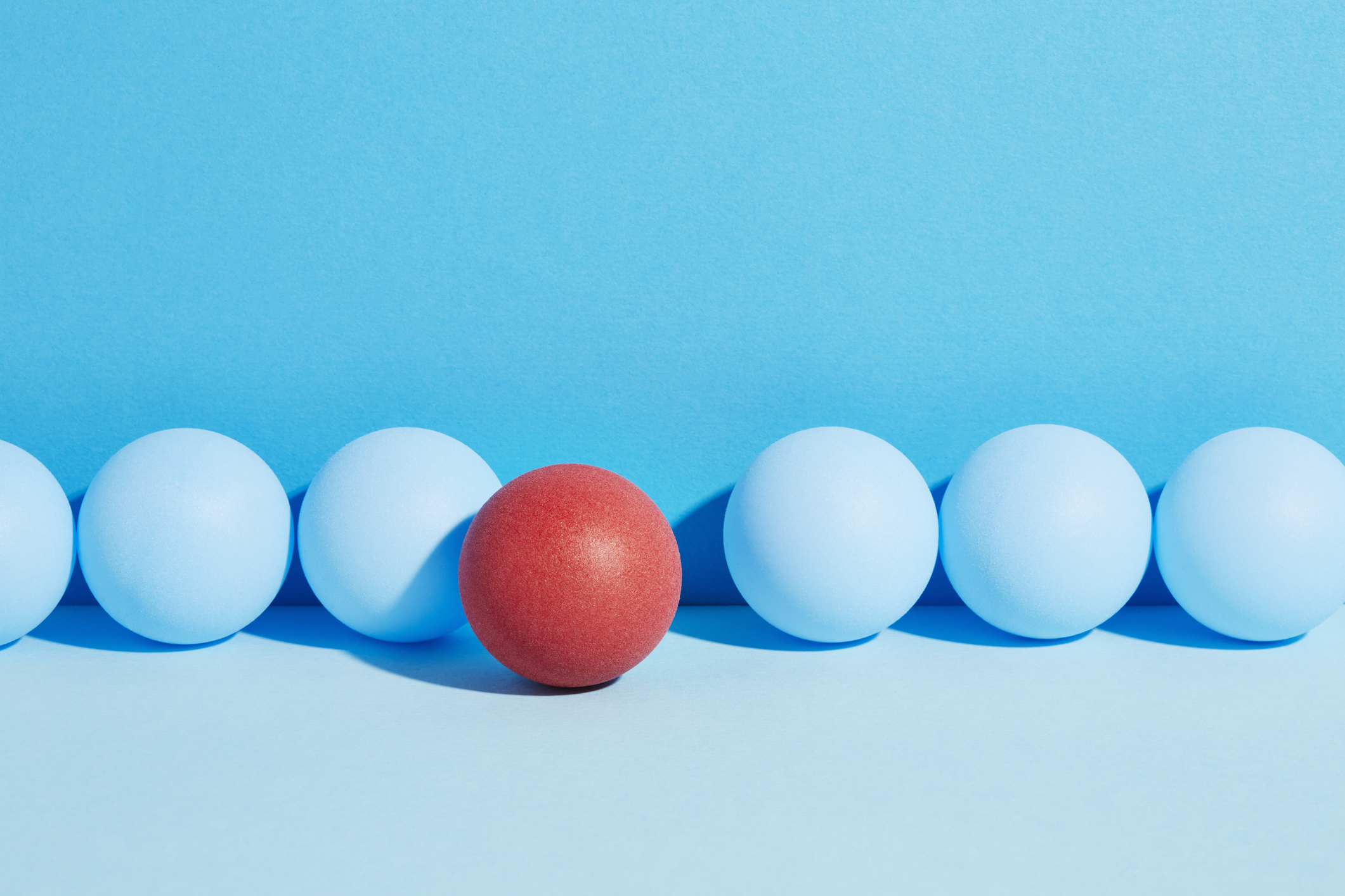 A red egg stands out from a group of blue eggs on a blue background, breaking the rule of conformity.