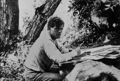 A man sitting at a table in the woods, resembling a scene from a Jack London novel.