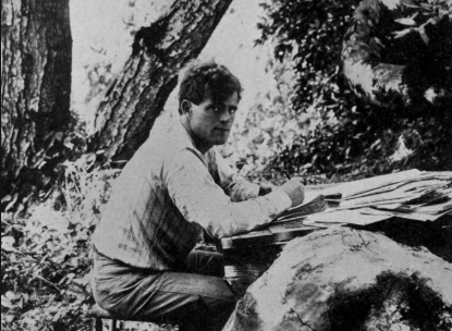 A man sitting at a table in the woods, resembling a scene from a Jack London novel.