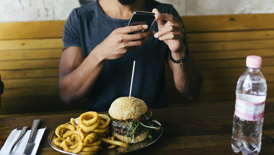 A man is still taking a picture of a burger on his phone.