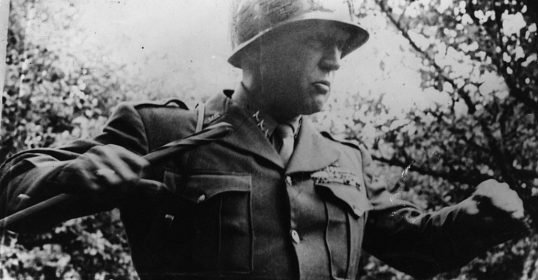 A man in a military uniform, resembling General Patton, holding a gun.