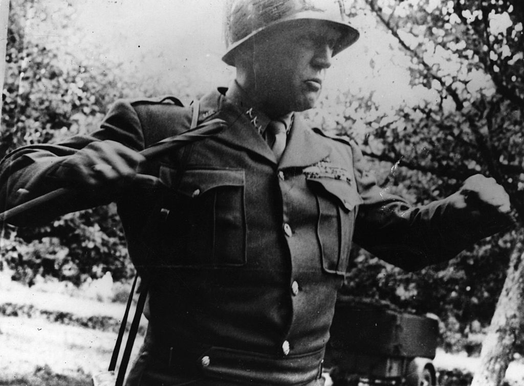 A man in a military uniform, resembling General Patton, holding a gun.