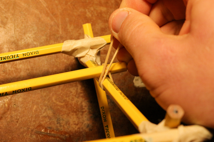 Attaching a pencil halfway up on the other side of the supports by rubber bands.