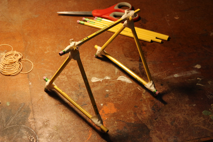 Boat like structure of pencils along with scissor and other pencils displayed on ground.