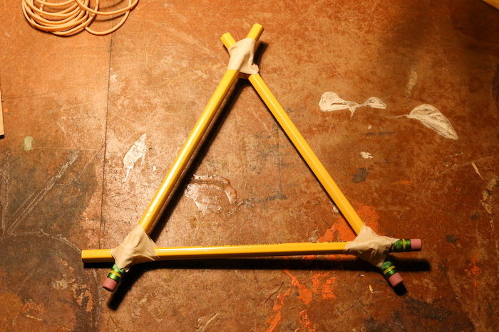 Pencils are attached with each other in a triangular shape with the help of tape.