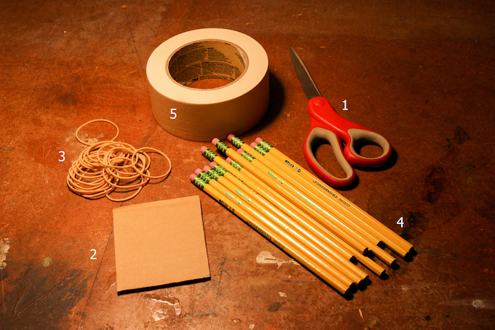 Accessories like pencils, Scissor, Tape, Rubber bands and card board displayed on the ground. 