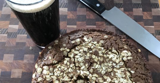 A slice of pie on a cutting board next to a glass of beer, perfect for celebrating St. Patrick's Day.
