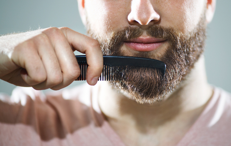 A man is grooming his beard with a comb as part of his routine.