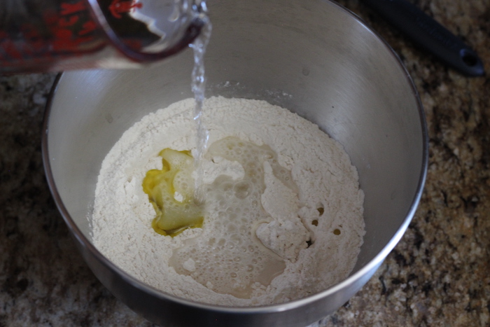 Water and oil being added to mixture containing yeast, flour, and salt. 