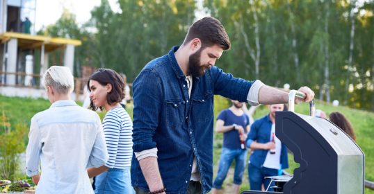 A man grilling while a group of people stands around.
