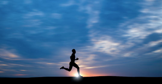 A silhouette of a man running on a hill at sunset, radiating happiness and embracing the connection with nature.