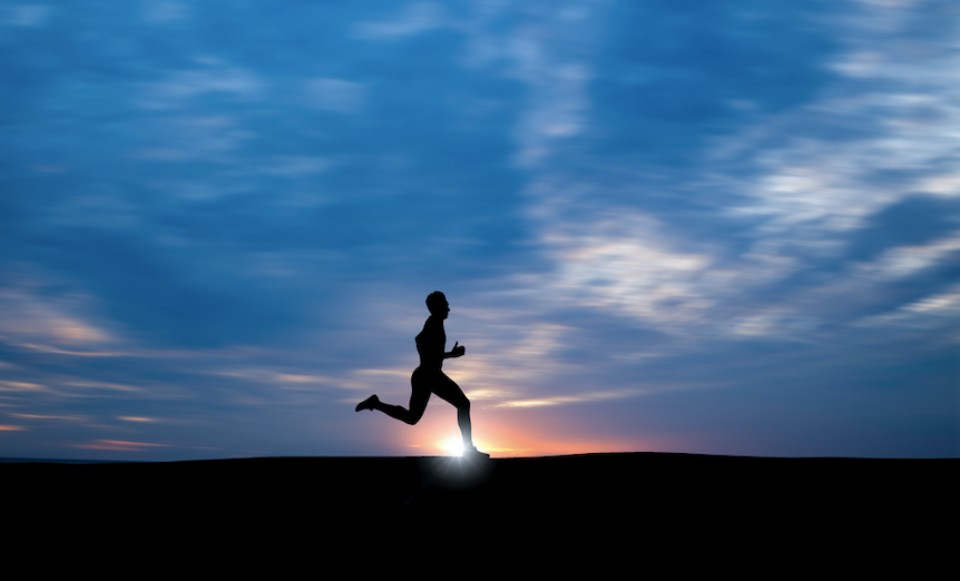 A silhouette of a man running on a hill at sunset, radiating happiness and embracing the connection with nature.
