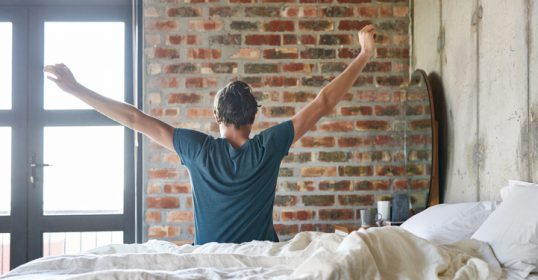 Waking up in bed with his arms raised, the man is ready to conquer the day.