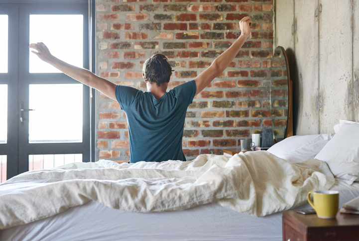 Waking up in bed with his arms raised, the man is ready to conquer the day.