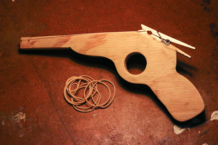 A wooden toy gun sits on a table, perhaps a kid's craft project.