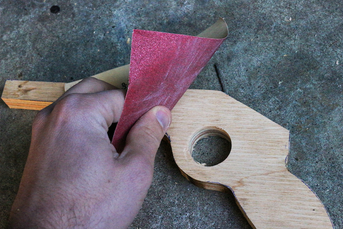 Sanding the plywood made gun with a piece of paper.