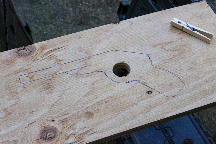 A hole in plywood having gun's image on it along the clothespin.