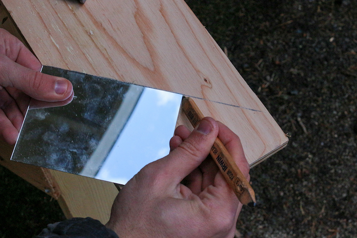 Marking the mirror with pencil placed on plywood.