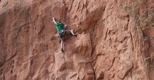 A man is climbing up the side of a rock wall, showcasing his physical intelligence and determination.