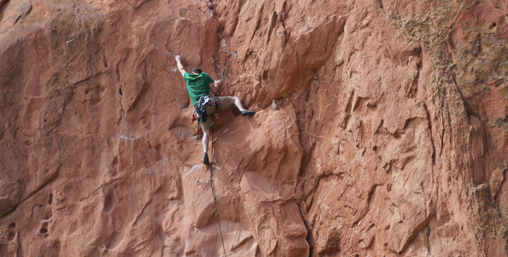 A man is climbing up the side of a rock wall, showcasing his physical intelligence and determination.