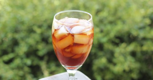 A glass of iced tea sits on a wooden table at home.