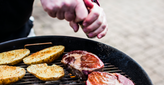 A person grilling steak and potatoes on a grill, showcasing their grilling techniques.