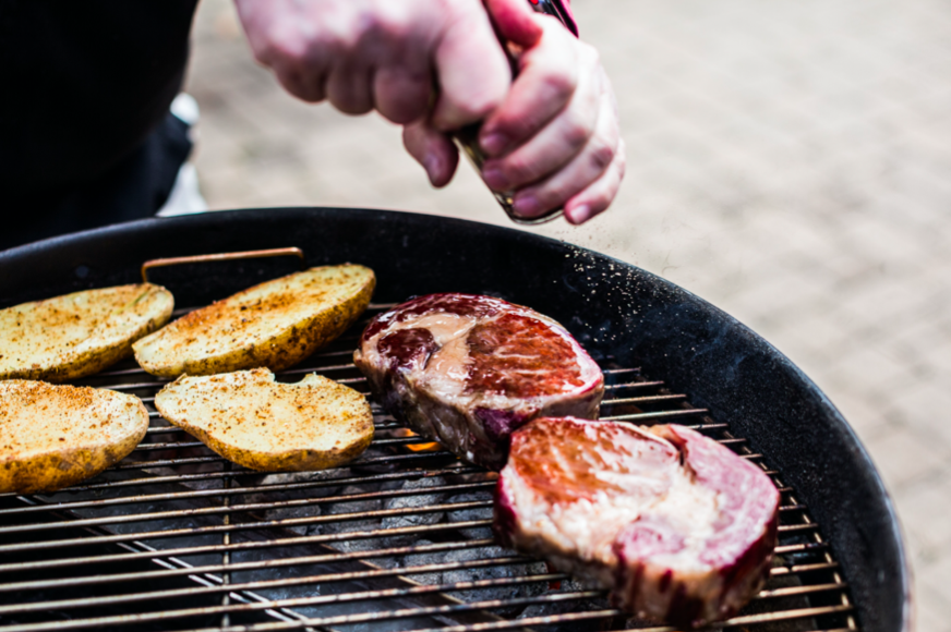 A person grilling steak and potatoes on a grill, showcasing their grilling techniques.