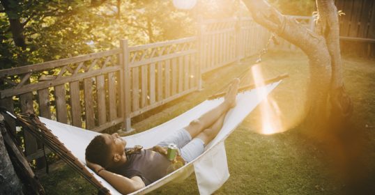 A man lounging in a hammock, listening to a podcast.