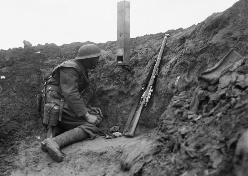 A soldier kneeling in a trench with a rifle uses a mirror periscope designed by kids for better visibility.